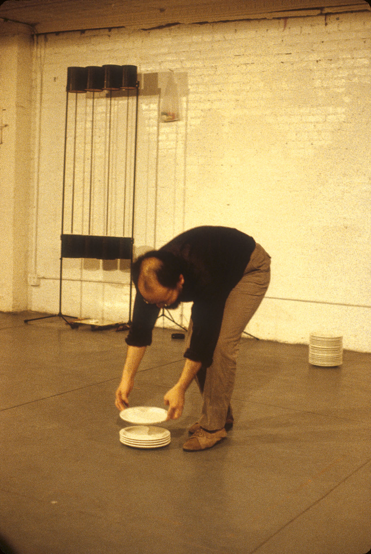 Photo of a man bending over and adding to a stack of plates on the floor.